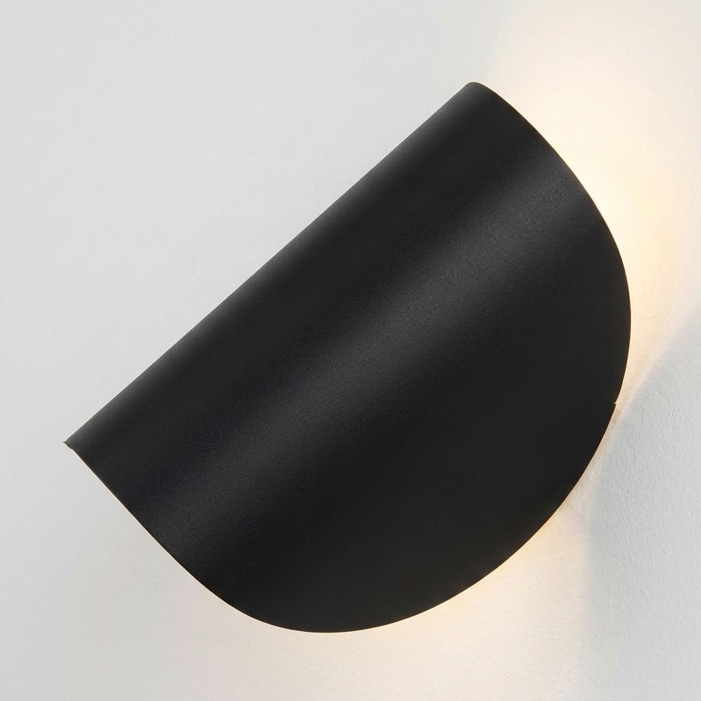 A modern matte black semi-circular wall sconce casting a warm light against a plain white wall.