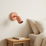 A peach pink wall sconce on a cream wall above a wooden nightstand, beside a beige sofa with soft cushions.