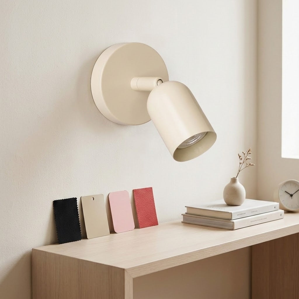 A cream wall sconce with a round backplate sits above a wooden console displaying colour samples, books and a small vase.