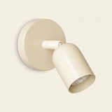 Cream wall sconce with a round backplate and downward-angled shade against an off-white background.