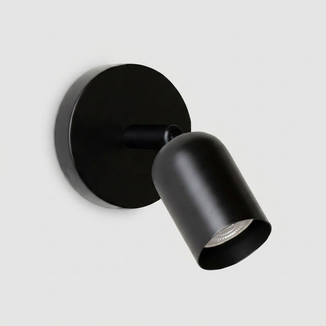 A modern matte black spotlight wall sconce with a circular backplate and adjustable cylindrical shade, shown against a light gray background.