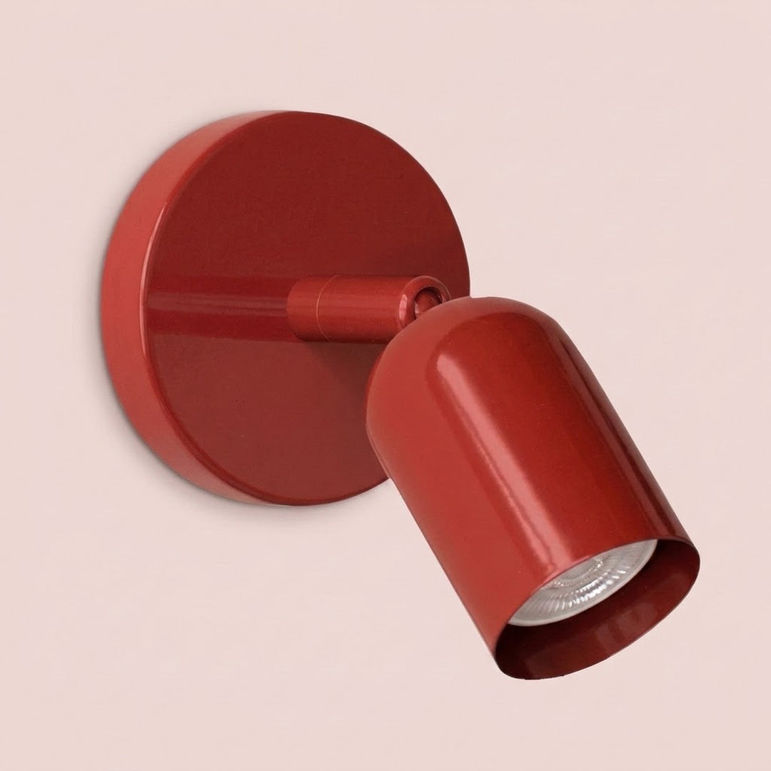 Close-up of a glossy red wall sconce with a round backplate and visible bulb against a pale pink background.