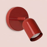Close-up of a glossy red wall sconce with a round backplate and visible bulb against a pale pink background.