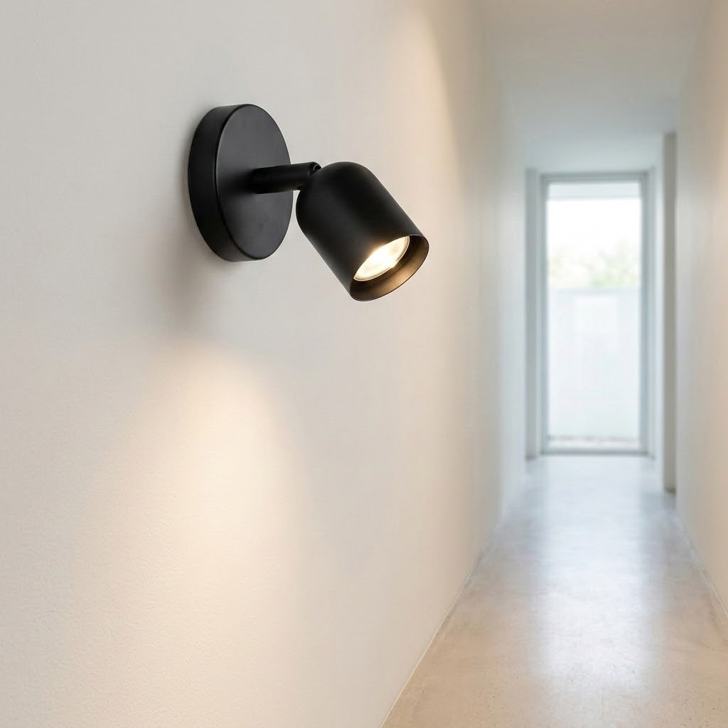 A matte black wall sconce lights up a bright white hallway with a warm, focused glow.