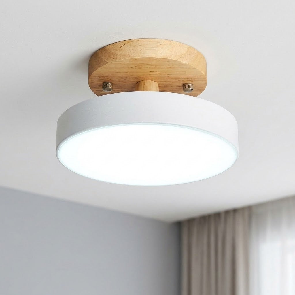 A modern semi-flush mount ceiling light with a white cylindrical shade and a natural wood circular ceiling mount, shown installed on a white ceiling in a room.