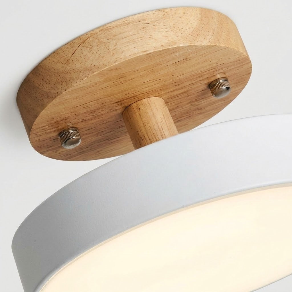 Close-up of a ceiling light fixture showing a round natural wood ceiling mount with two metal screws and a white cylindrical shade below.