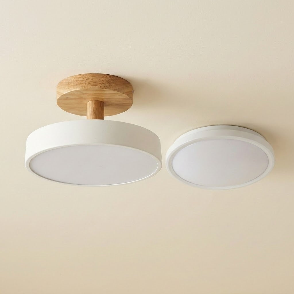 A modern ceiling light fixture shown from below, featuring a circular white shade with a natural wood ceiling mount and a second matching round light element to the right, set against a plain beige wall.