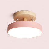 A modern semi-flush mount ceiling light with a pink cylindrical shade and a natural wood ceiling mount, shown illuminated against a soft pink background.