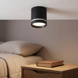 Black cylindrical LED downlight with a silver-colored band glows above a bedside table beside a bed.