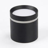 Black cylindrical LED downlight rests diffuser-side up on a white background, showing its silver-colored band and circular white diffuser.