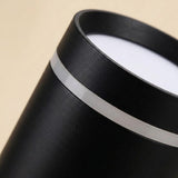 Close-up of a black LED downlight shows its textured housing, silver-colored band, and white diffuser against a beige background.