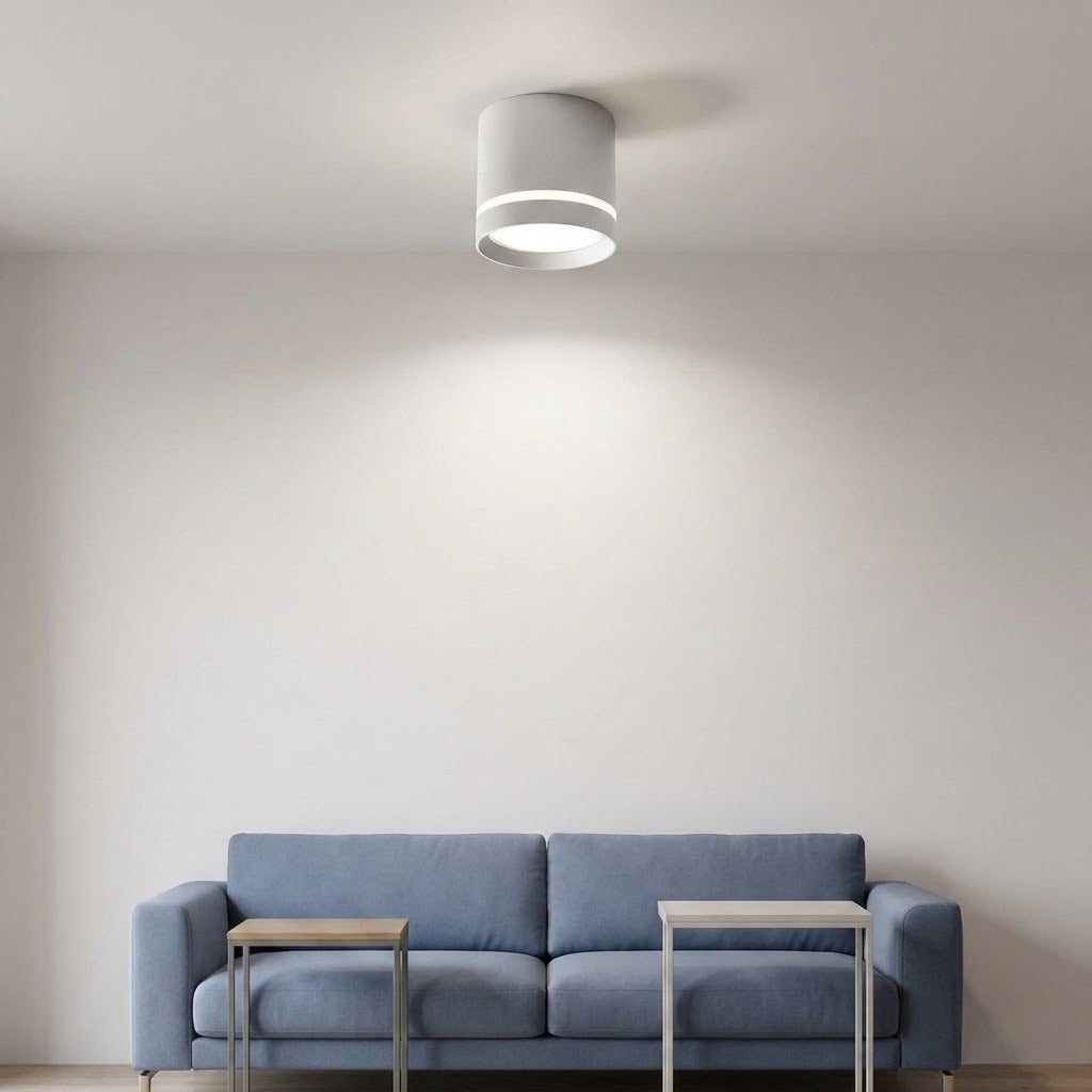 A white cylindrical LED downlight with a glowing accent ring illuminates a living room above a blue sofa.