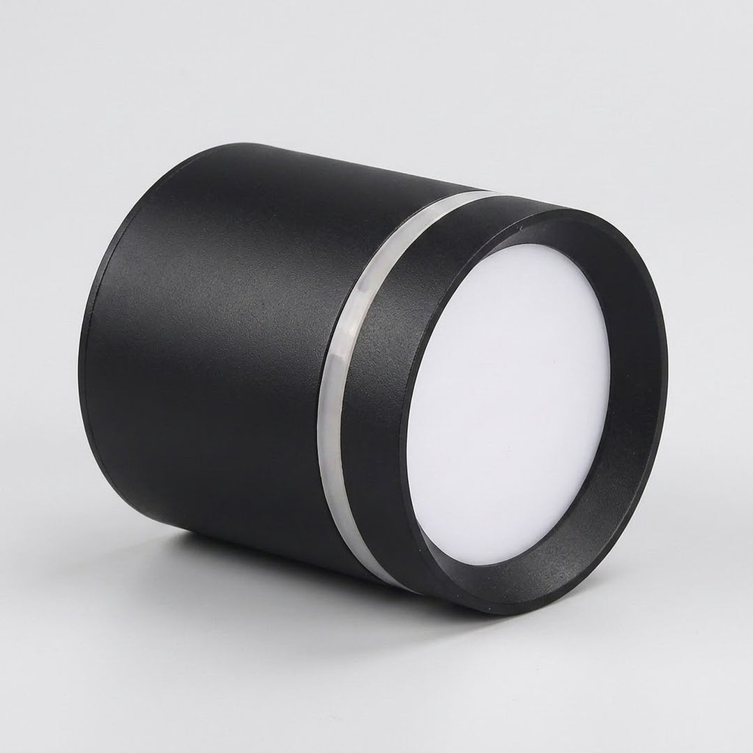 A black cylindrical LED downlight rests on a light gray surface, with its white diffuser facing right and silver trim visible.