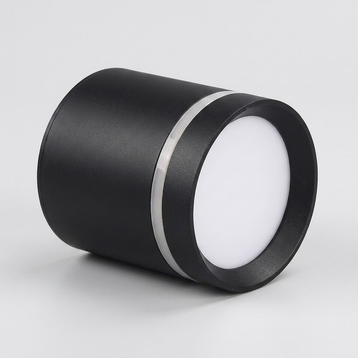 A black cylindrical LED downlight rests on a light gray surface, with its white diffuser facing right and silver trim visible.