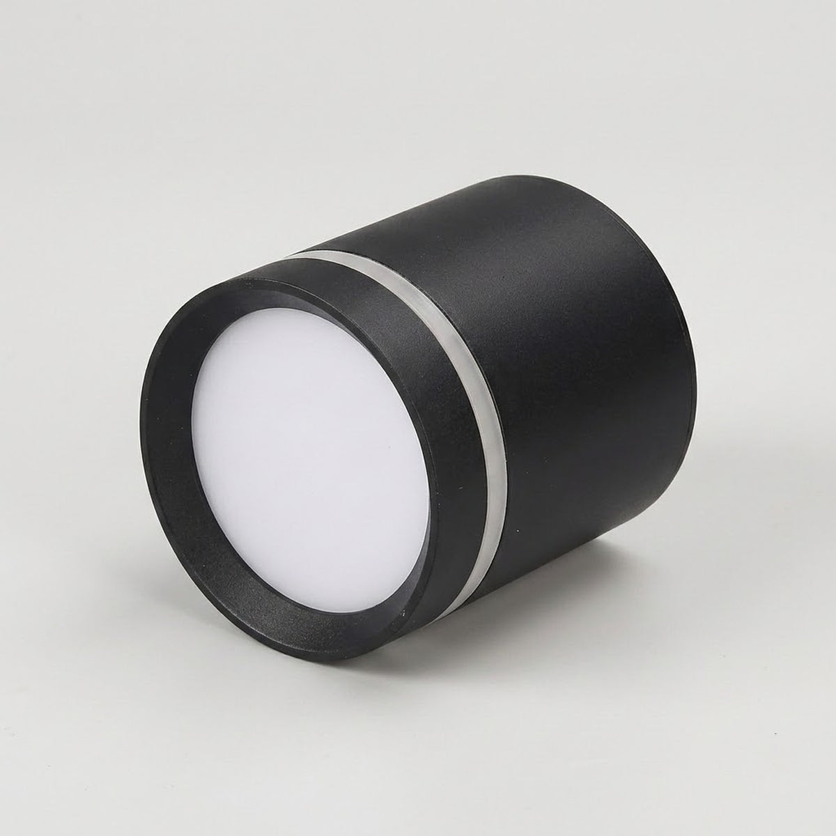 A black cylindrical LED downlight sits angled on its side against a light gray background, showing a white diffuser and silver trim.