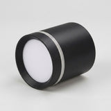 A matte black LED downlight lies sideways against a light gray background, with its white diffuser facing left and silver trim visible.
