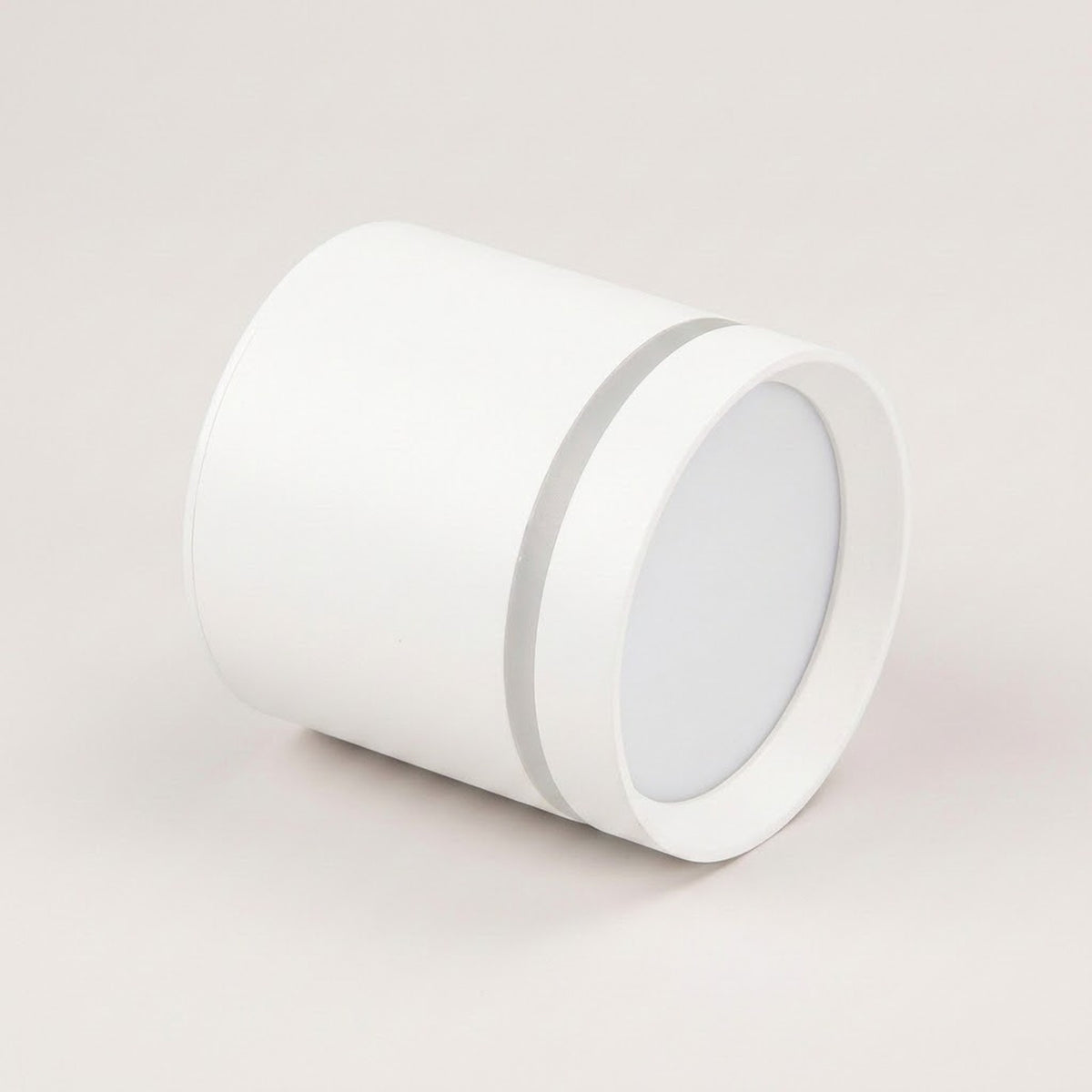 A white cylindrical LED downlight rests on a pale beige background, showing its recessed circular diffuser and silver-colored accent ring.