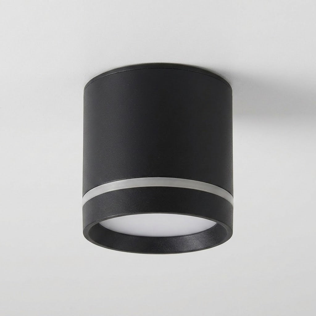 A black cylindrical LED downlight with a silver-colored accent ring and white diffuser is mounted on a pale ceiling.