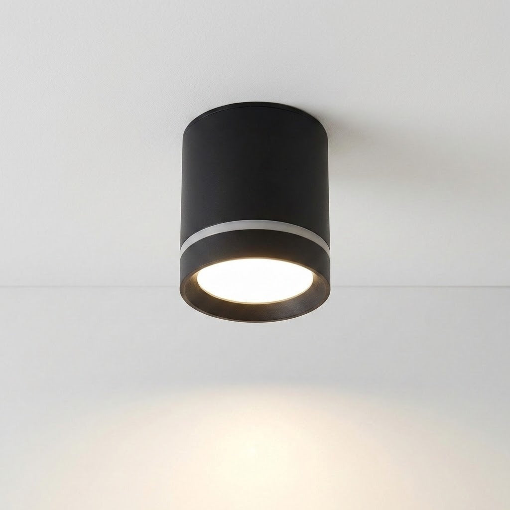 A black cylindrical LED downlight with a silver-colored accent ring casts warm light beneath a white ceiling.