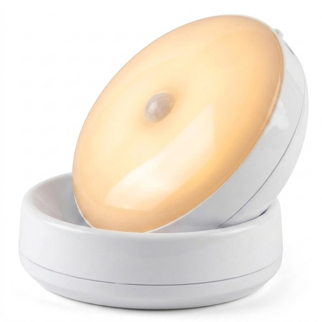 A white night light with a warm glowing face tilts upward in its matching round base against a white background.