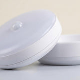 Close-up of a white night light showing its smooth casing, frosted face, and clear motion sensor against a pale background.