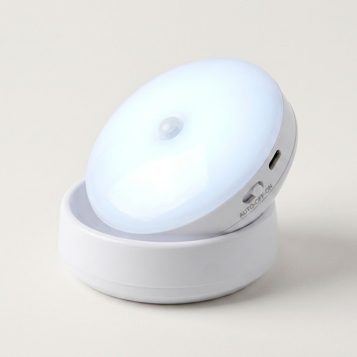 A white night light glows cool white in its matching base, with a charging port and sliding switch visible against a pale background.