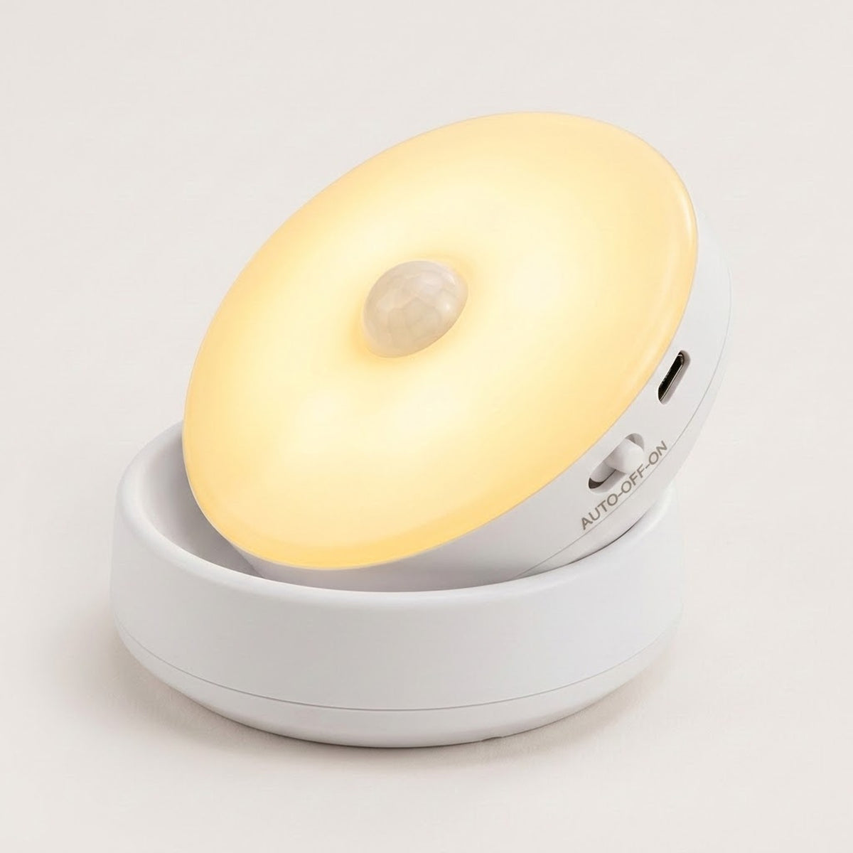 A small white portable LED night light with a circular glowing lamp and a built-in motion sensor, shown on a clean light gray background.