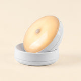 A white night light with a warm yellow glow rests tilted in its matching base against a light cream background.