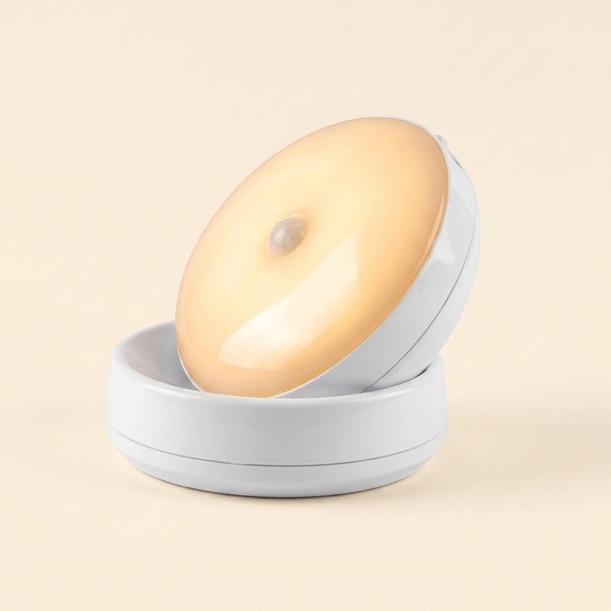 A white night light with a warm yellow glow rests tilted in its matching base against a light cream background.