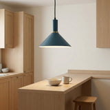 A modern pendant light with a matte dark teal-blue cone shade and a gold-toned collar, hanging over a light wood kitchen island with a bowl and mug on the counter.