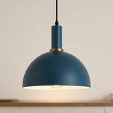 A modern dome-shaped pendant light in matte blue with a gold accent ring and a black hanging cord, shown illuminated against a warm off-white background.