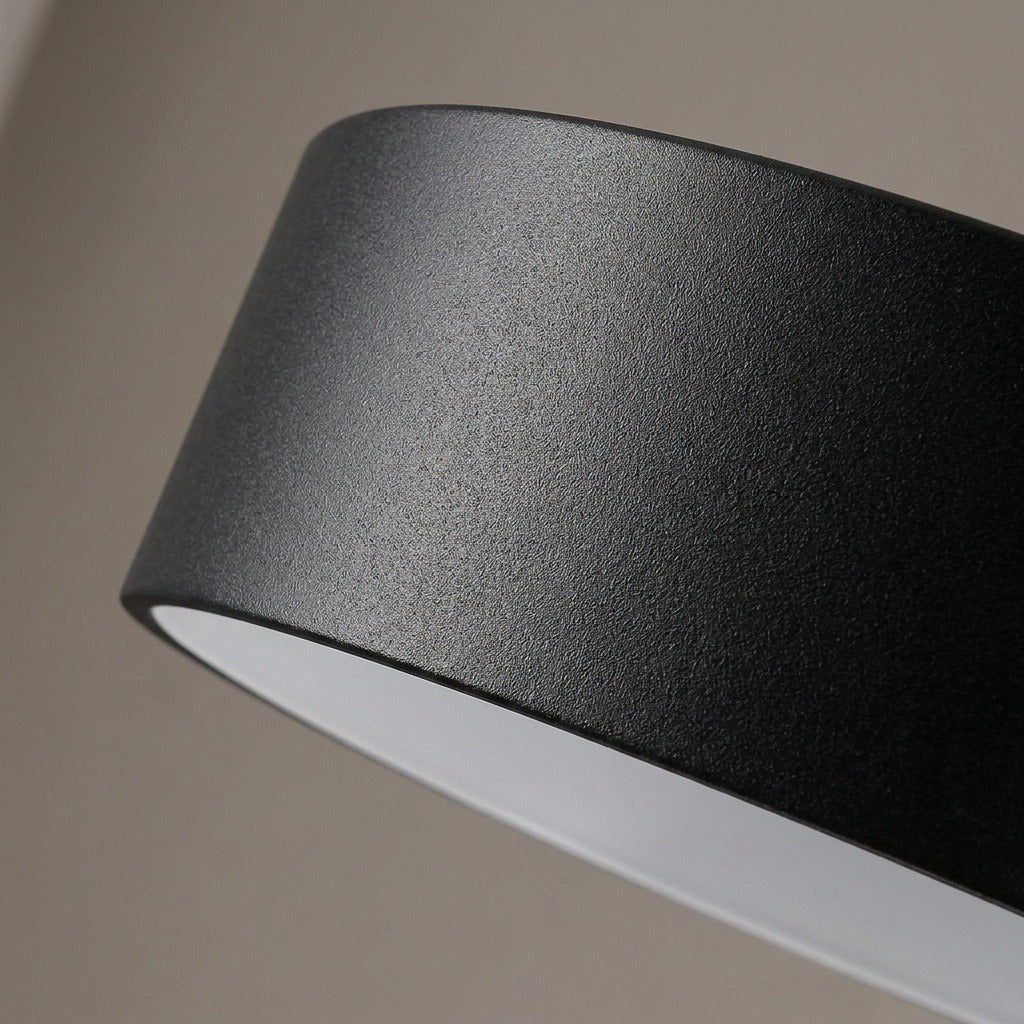 Close-up of a black pendant light’s textured painted metal shade and white interior against a neutral background.
