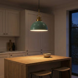 A modern pendant light with a muted teal-green dome shade and brass hardware hangs over a wooden kitchen island in a dimly lit kitchen setting.