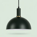 A matte black dome pendant light with a gold accent ring and a white interior, suspended against a pale green background.