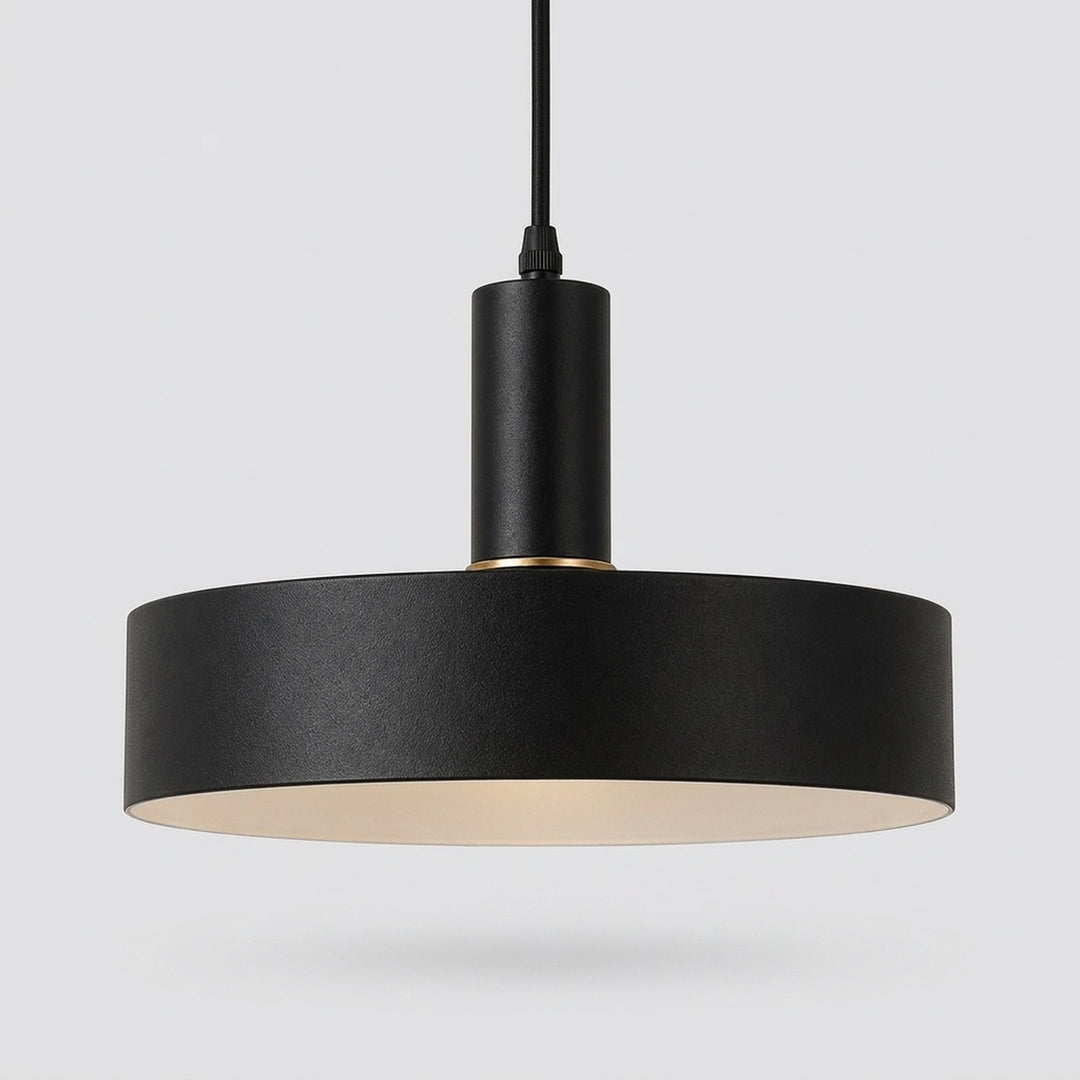 A modern black pendant light with a wide cylindrical shade, a matte black metal body, and a warm cream-colored interior, suspended against a light gray background.