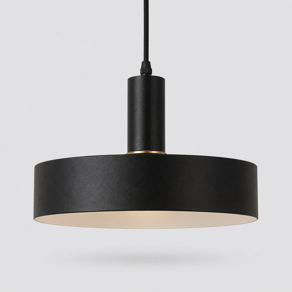 A modern black pendant light with a wide cylindrical shade, a matte black metal body, and a warm cream-colored interior, suspended against a light gray background.