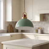 A modern pendant light with a muted sage green dome shade, a white interior, and brass hardware hanging over a kitchen island.