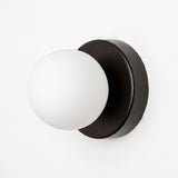 A wall sconce with a black circular iron base and white plastic globe shade is shown against a plain white background.