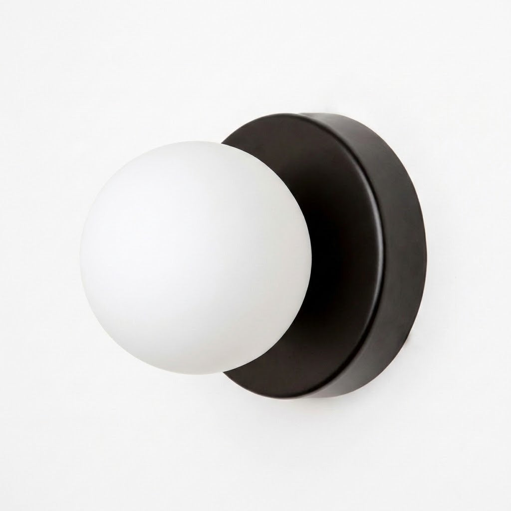A wall sconce with a black circular iron base and white plastic globe shade is shown against a plain white background.