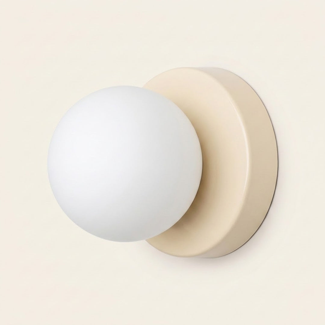 Wall sconce viewed at an angle with a white globe shade and cream circular base against a pale background.
