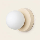 Wall sconce viewed at an angle with a white globe shade and cream circular base against a pale background.