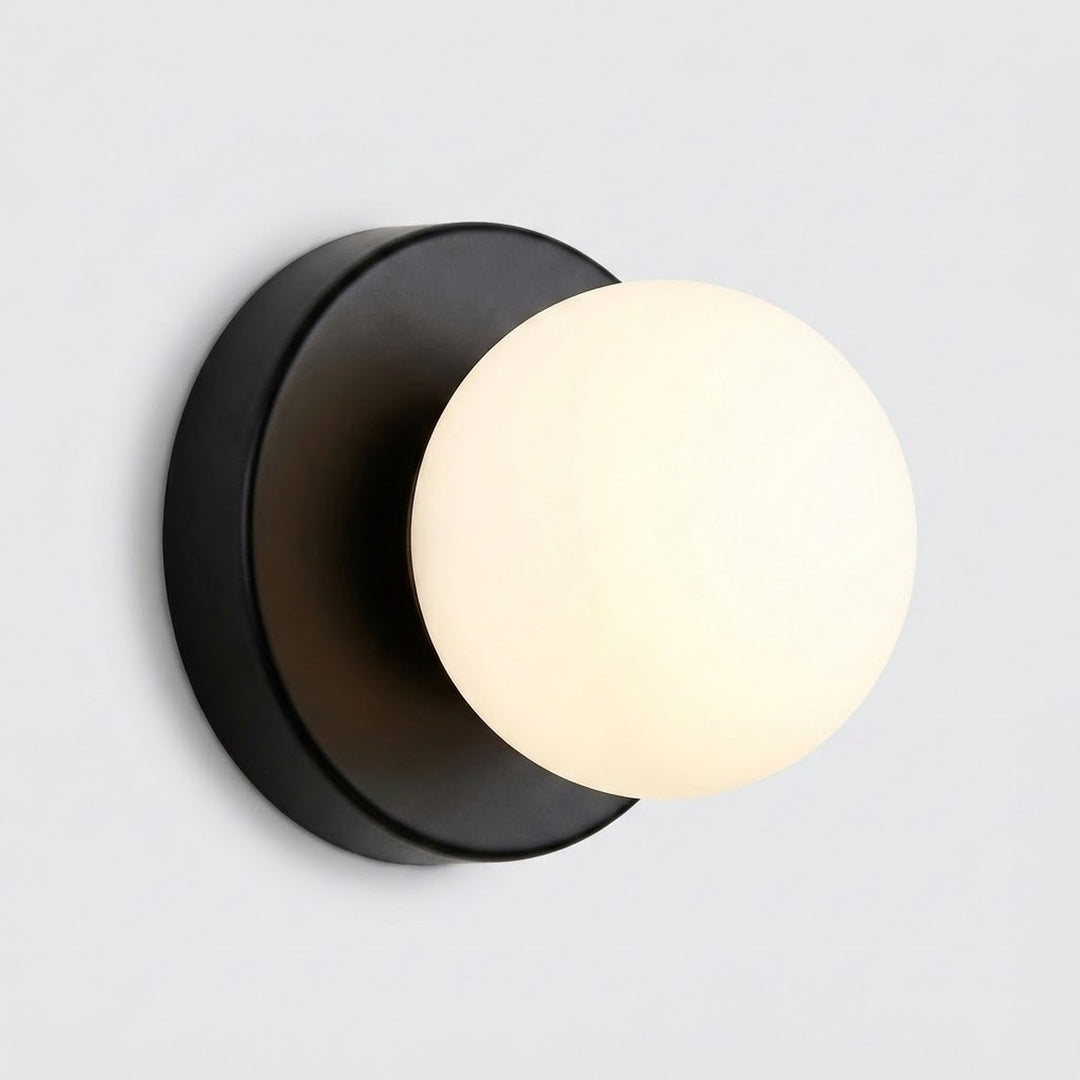 Wall sconce with a warmly glowing plastic globe shade and black circular iron base against a light gray background.