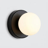 Wall sconce with a warmly glowing plastic globe shade and black circular iron base against a light gray background.