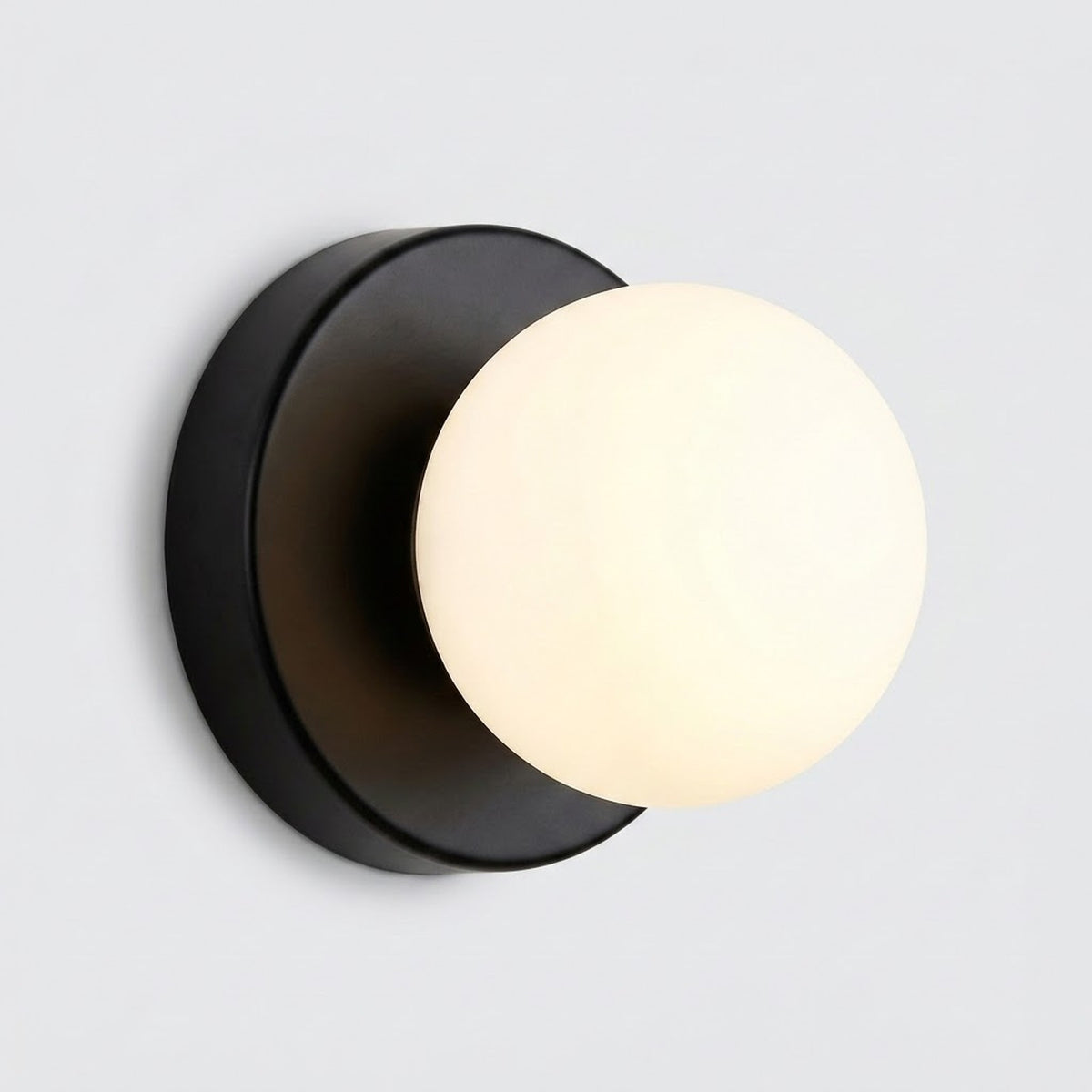 Wall sconce with a warmly glowing plastic globe shade and black circular iron base against a light gray background.