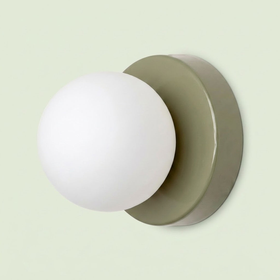 Wall sconce with a white plastic globe shade and muted green circular iron base against a pale green background.