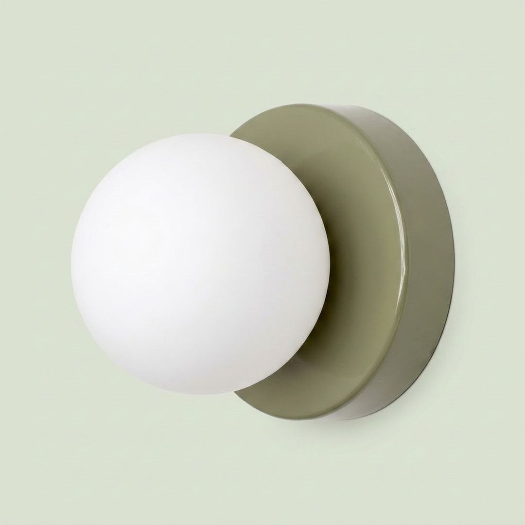 Wall sconce with a white plastic globe shade and sage green circular iron base against a pale green background.
