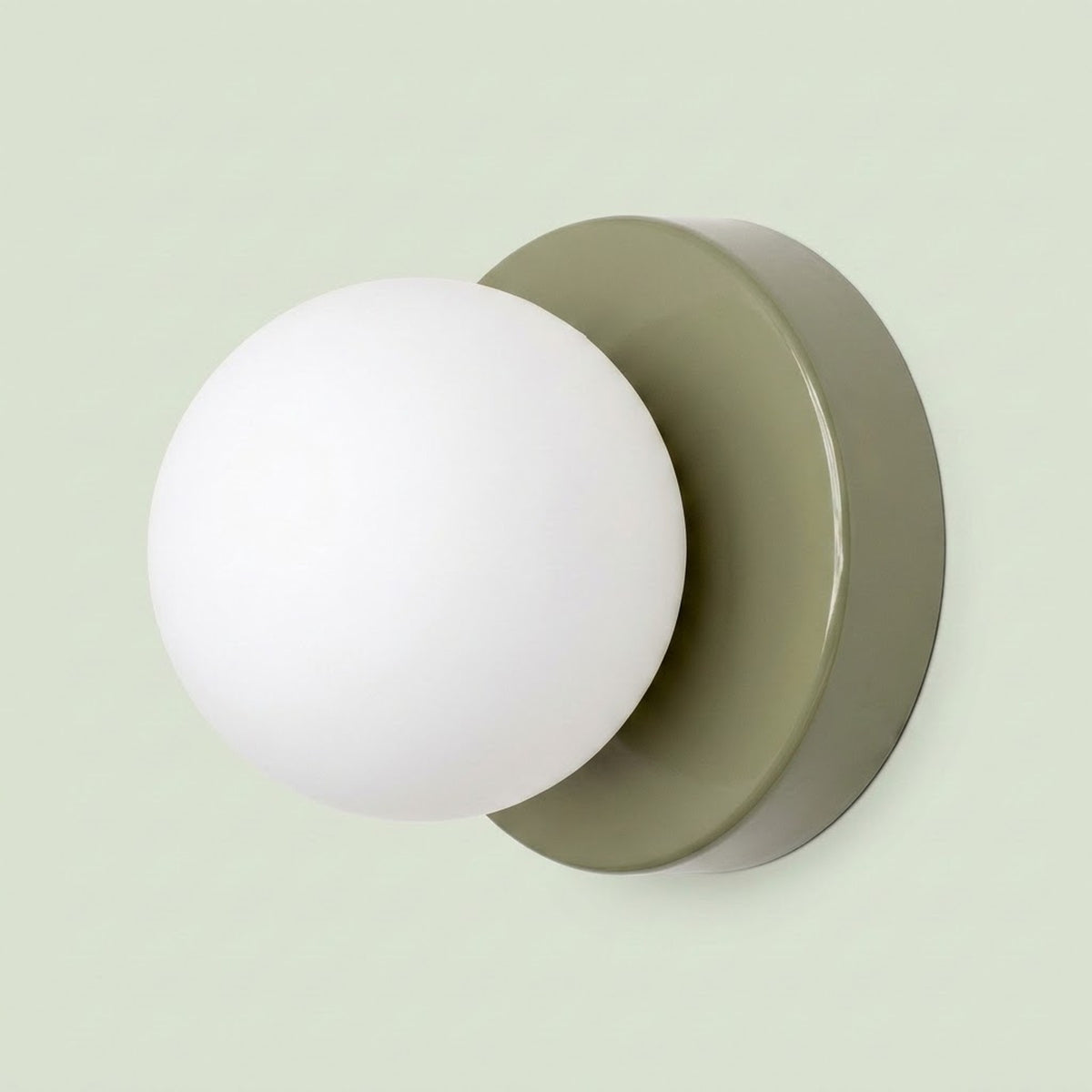 Wall sconce with a white plastic globe shade and sage green circular iron base against a pale green background.