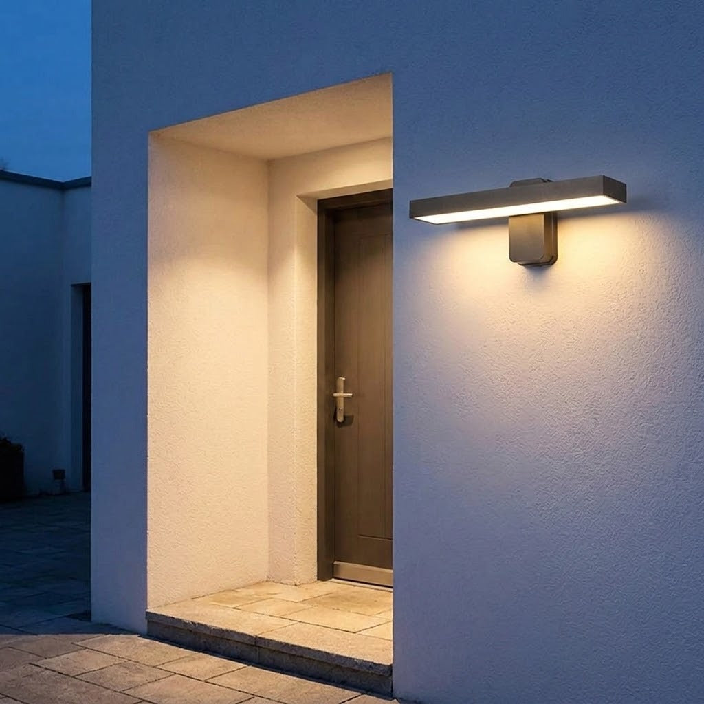 Dark rectangular wall sconce casts warm white light across a textured exterior wall and recessed doorway at dusk.