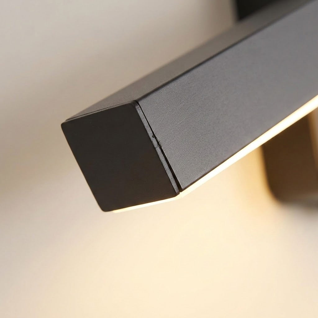 Close-up of the wall sconce shows its dark textured housing, squared end cap, and warm light against a beige wall.