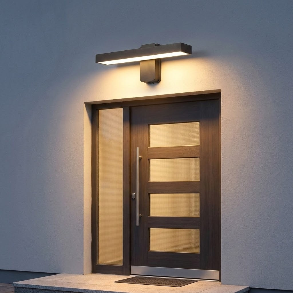 Dark horizontal wall sconce casts warm white light above a wooden front door and glazed sidelight at dusk.